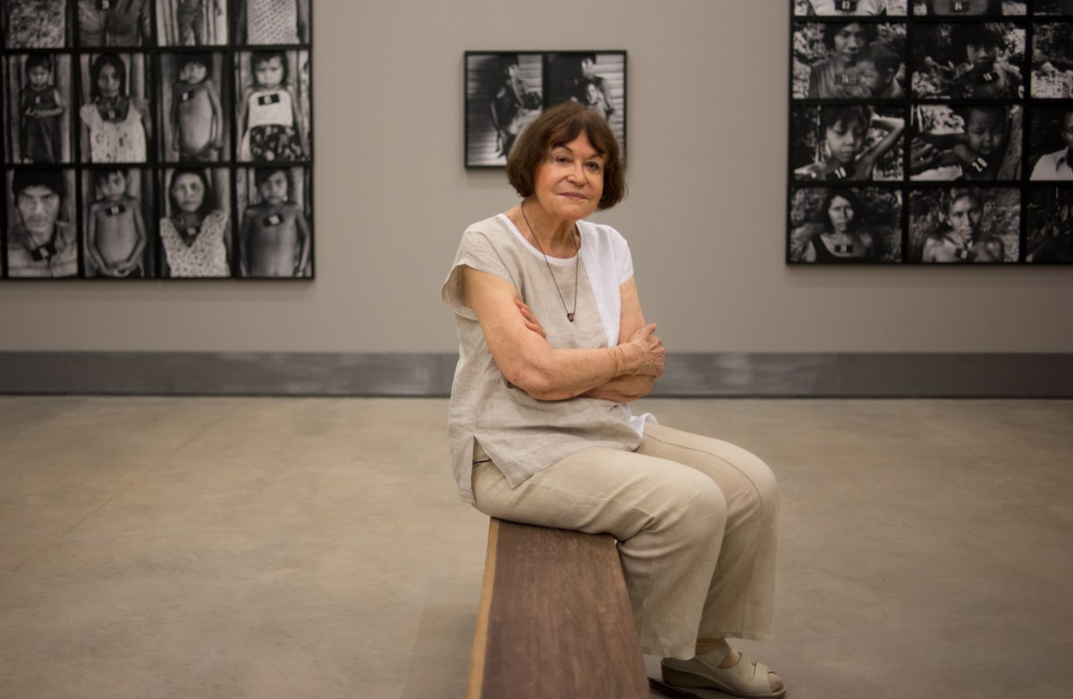 Claudia Andujar sentada em uma sala de exposição, diante de suas fotografias.